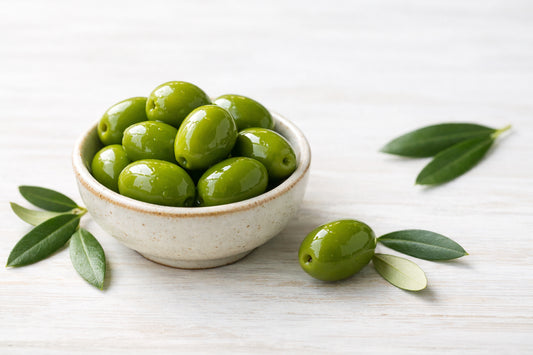 Green Olives — vibrant green olives in a ceramic bowl with olive leaves on a light wooden surface