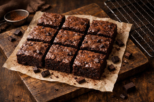 Belbake Brownie Mix — freshly baked fudgy brownies dusted with cocoa powder on a wooden board.