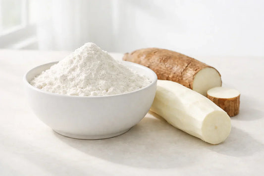 Cassava flour — a white ceramic bowl filled with fine flour next to a peeled cassava root on a clean surface.