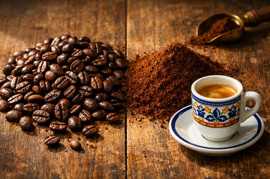 Delta Café koffiebonen vs gemalen — Whole coffee beans next to a pile of ground coffee on a wooden table with an espresso cup.
