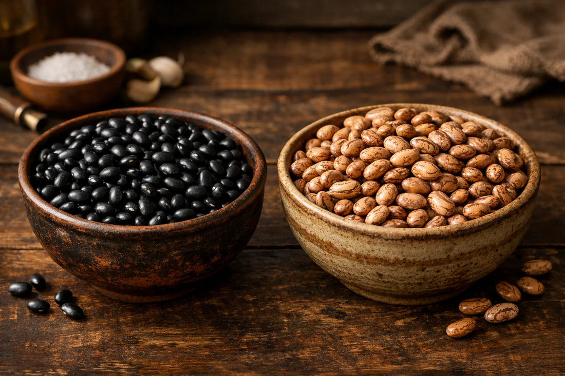 Fejão Preto vs Fejão Carioca — two bowls on a wooden table, one with black beans and one with pinto beans.