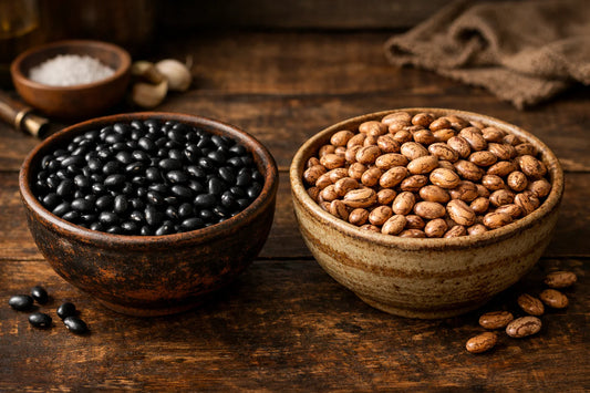 Fejão Preto vs Fejão Carioca — two bowls on a wooden table, one with black beans and one with pinto beans.
