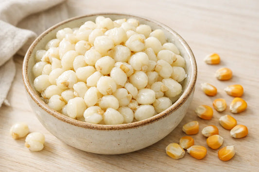 White Hominy Corn grain — cooked hominy corn in a bowl on a light wooden surface